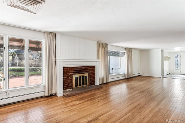 unfurnished living room with light hardwood / wood-style floors, a baseboard radiator, and a brick fireplace