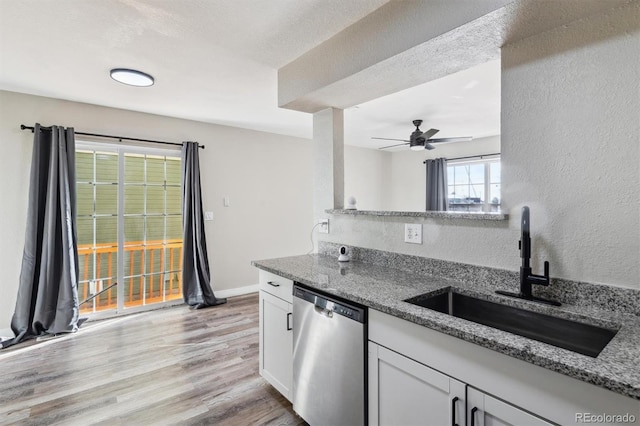 kitchen featuring white cabinets, sink, stainless steel dishwasher, light wood-type flooring, and stone countertops