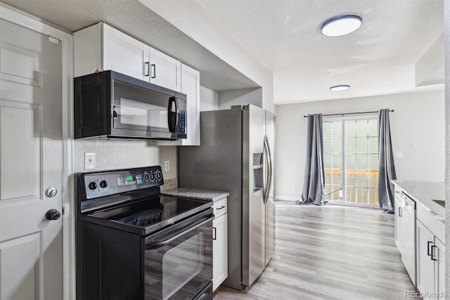 kitchen with light wood-type flooring, light stone counters, a textured ceiling, black range with electric cooktop, and white cabinetry