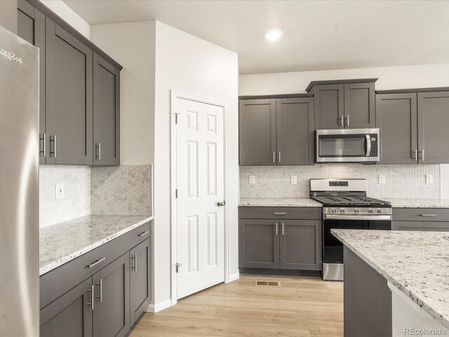 kitchen with decorative backsplash, stainless steel appliances, light stone counters, and light hardwood / wood-style floors