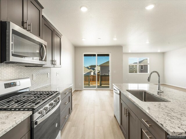 kitchen with light stone countertops, appliances with stainless steel finishes, light wood-type flooring, dark brown cabinets, and sink