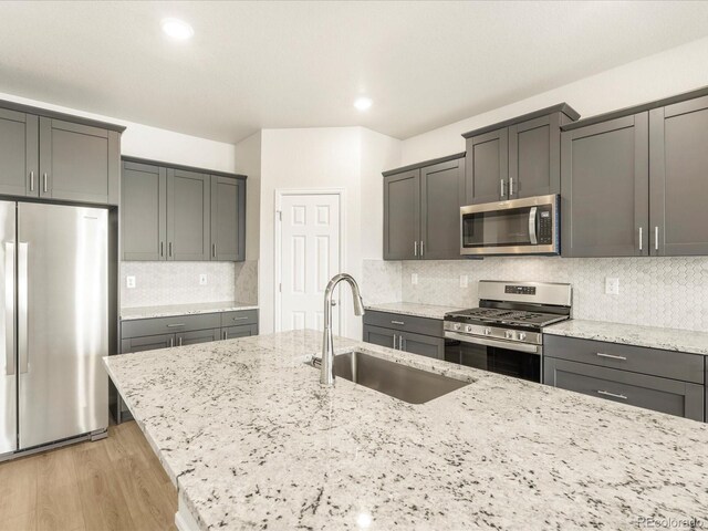 kitchen with light stone counters, light hardwood / wood-style floors, sink, and stainless steel appliances