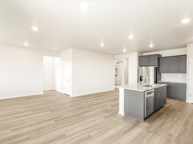 kitchen featuring stainless steel appliances, gray cabinets, light hardwood / wood-style floors, and an island with sink