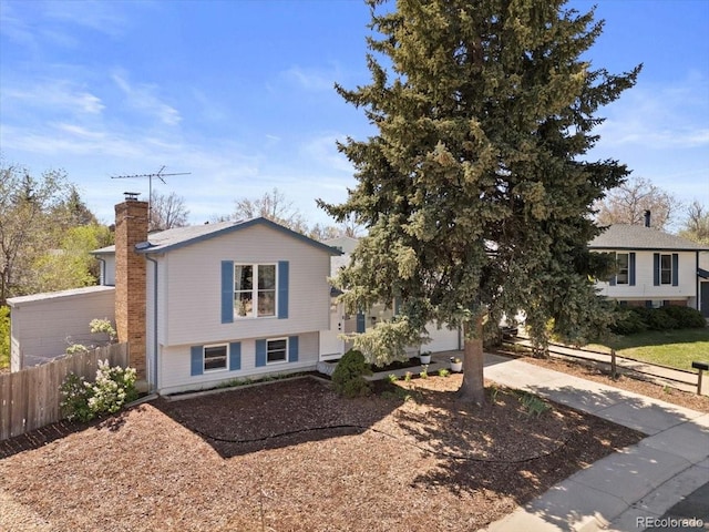 split level home featuring a chimney, fence, concrete driveway, and a garage
