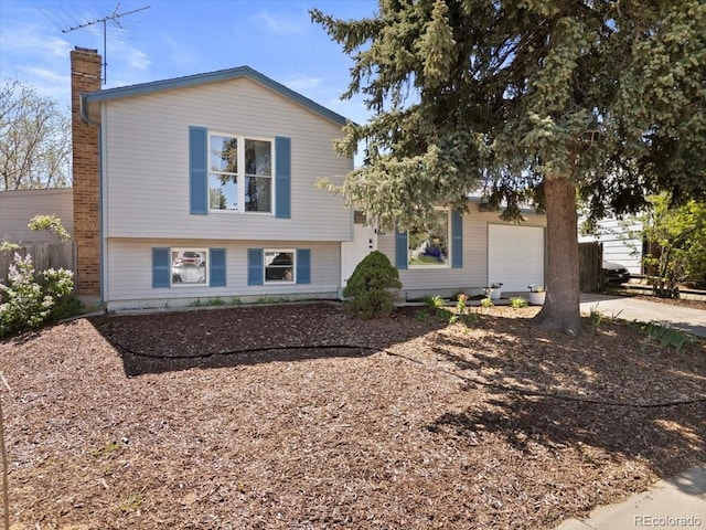 split level home with a chimney, an attached garage, and concrete driveway