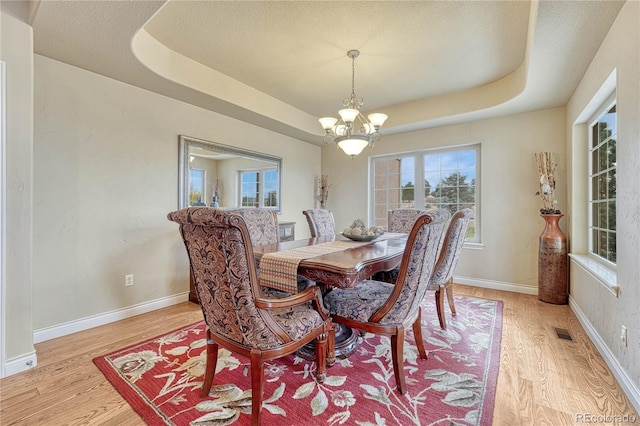 dining room with light hardwood / wood-style floors, a textured ceiling, a raised ceiling, and an inviting chandelier