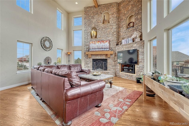 living room featuring a stone fireplace, light hardwood / wood-style floors, and a towering ceiling