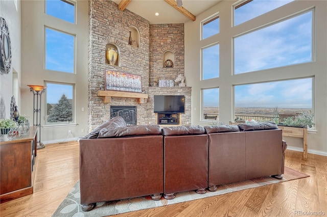 living room featuring light hardwood / wood-style flooring, a fireplace, beamed ceiling, and a towering ceiling