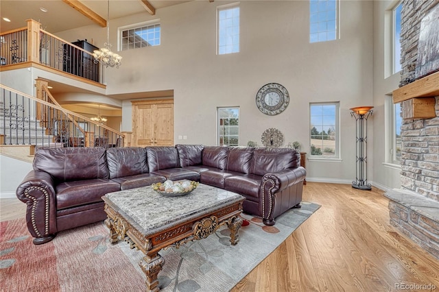 living room featuring an inviting chandelier, beam ceiling, light wood-type flooring, and a towering ceiling