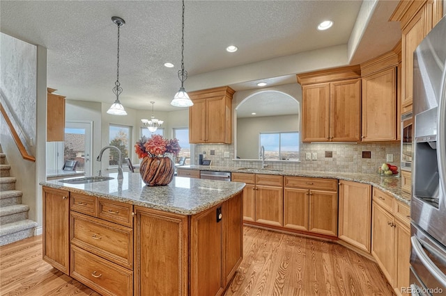 kitchen featuring a kitchen island with sink, light hardwood / wood-style flooring, a textured ceiling, and decorative light fixtures