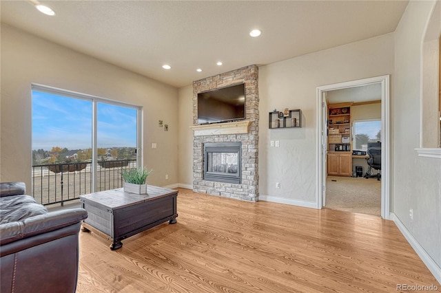 living room with light hardwood / wood-style floors, a stone fireplace, and plenty of natural light