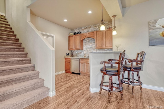 kitchen featuring light stone counters, a breakfast bar area, hanging light fixtures, light hardwood / wood-style flooring, and dishwasher