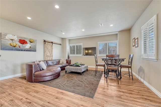 living room featuring a barn door, light hardwood / wood-style floors, and a textured ceiling