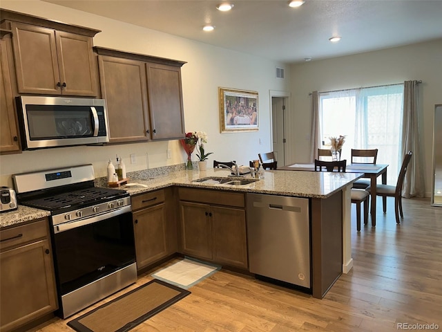 kitchen with light wood-type flooring, kitchen peninsula, appliances with stainless steel finishes, and sink