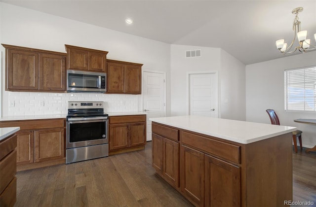 kitchen with appliances with stainless steel finishes, a kitchen island, tasteful backsplash, hanging light fixtures, and dark wood-type flooring