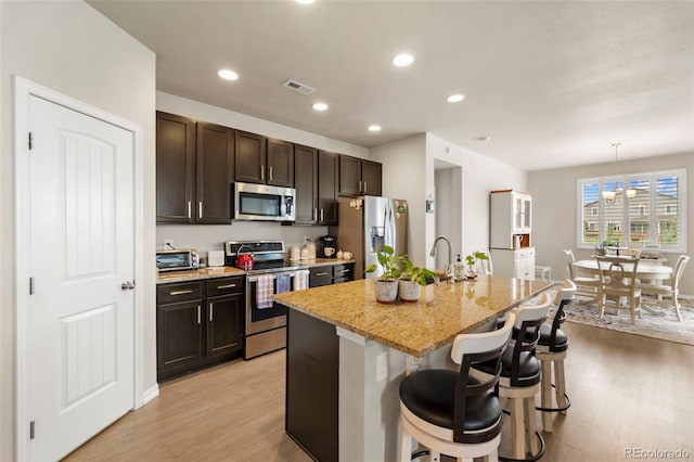 13138 Stoney Meadows Way, Peyton, CO 80831 - kitchen with appliances with stainless steel finishes, light wood-style flooring, a center island with sink, a breakfast bar area, and dark brown cabinets