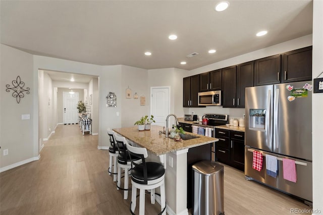 13138 Stoney Meadows Way, Peyton, CO 80831 - kitchen featuring appliances with stainless steel finishes, light wood-style floors, a kitchen bar, an island with sink, and light stone countertops
