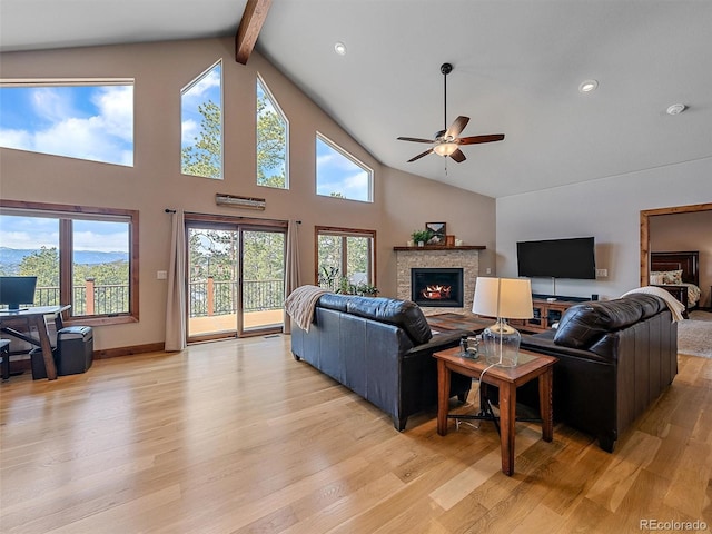 living area with beamed ceiling, a lit fireplace, a ceiling fan, and light wood finished floors