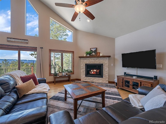 living area featuring baseboards, ceiling fan, light wood-type flooring, a glass covered fireplace, and high vaulted ceiling