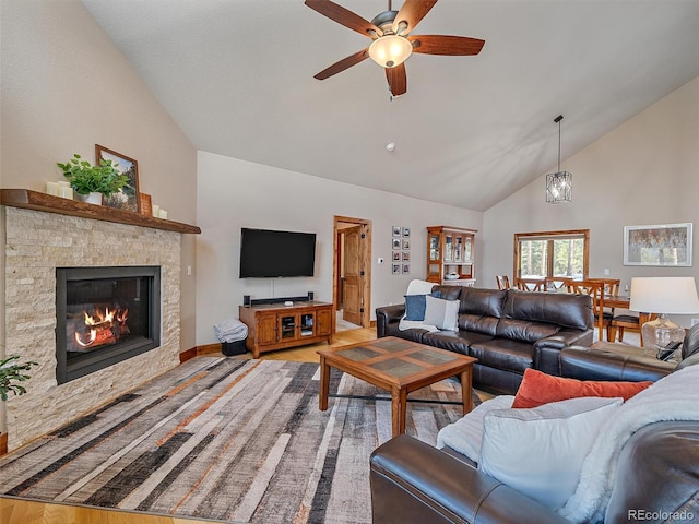 living room featuring high vaulted ceiling, light wood-style flooring, a stone fireplace, baseboards, and ceiling fan