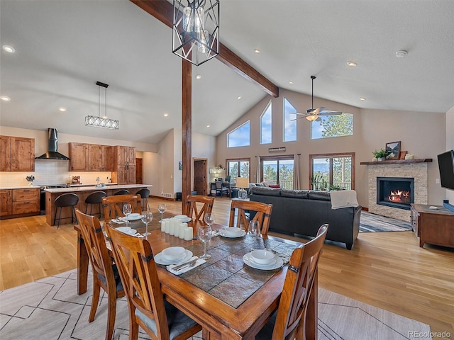 dining space featuring beam ceiling, high vaulted ceiling, light wood-style flooring, recessed lighting, and a fireplace