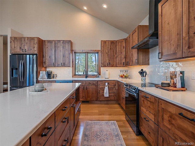 kitchen with black electric range oven, a sink, stainless steel fridge, brown cabinetry, and wall chimney range hood