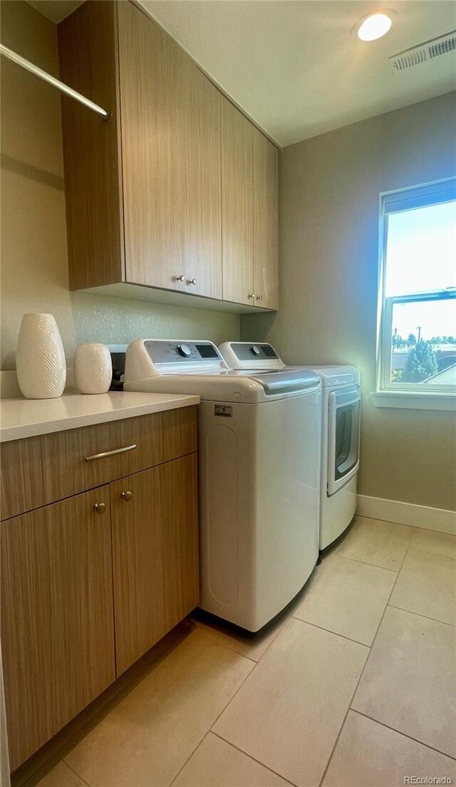 clothes washing area featuring light tile patterned flooring, visible vents, baseboards, cabinet space, and washer and clothes dryer