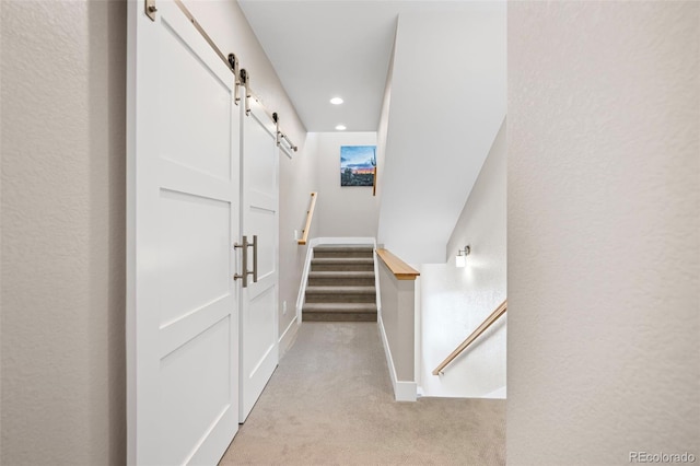 hallway featuring light carpet, a barn door, recessed lighting, and a textured wall