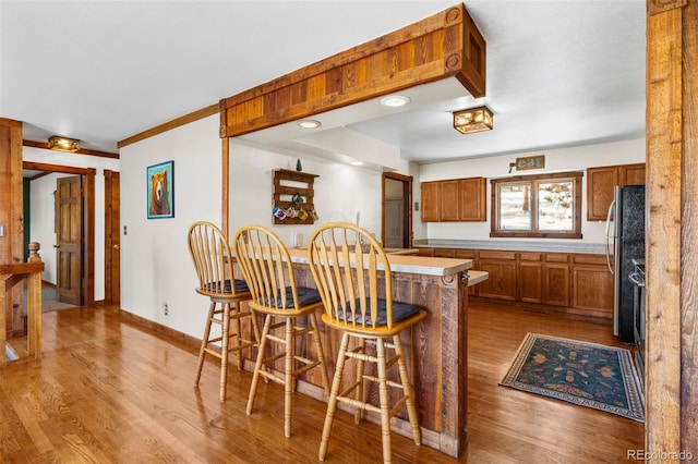 kitchen with kitchen peninsula, stainless steel fridge, a kitchen breakfast bar, light wood-type flooring, and ornamental molding