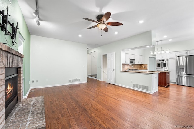 9365 Erminedale Dr, Lone Tree, CO 80124 - unfurnished living room featuring a brick fireplace, a ceiling fan, recessed lighting, wood finished floors, and rail lighting