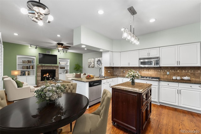9365 Erminedale Dr, Lone Tree, CO 80124 - kitchen featuring stainless steel appliances, ceiling fan, a peninsula, a brick fireplace, and open floor plan