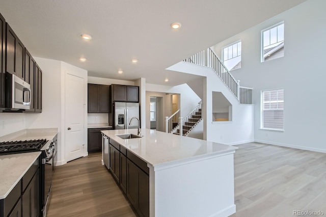 4588 Thistle Dr, Brighton, CO 80601 - kitchen with stainless steel appliances, a sink, light wood-style flooring, dark brown cabinetry, and a center island with sink