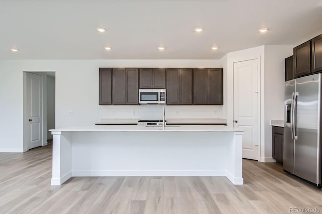 4588 Thistle Dr, Brighton, CO 80601 - kitchen featuring stainless steel appliances, light countertops, light wood-style flooring, a kitchen island with sink, and dark brown cabinets