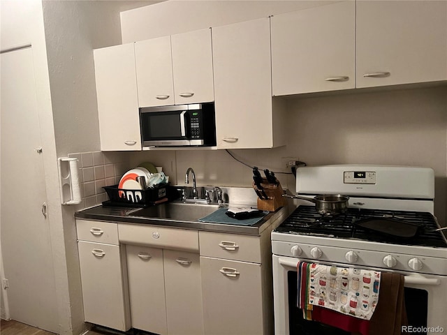 kitchen featuring white range with gas stovetop, white cabinets, sink, decorative backsplash, and wood-type flooring