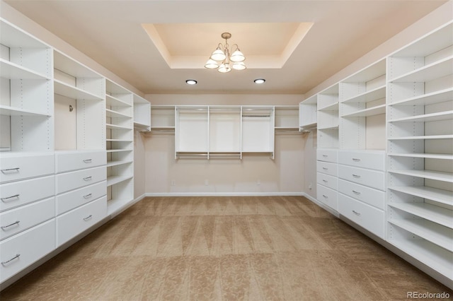 walk in closet featuring light carpet, a raised ceiling, and a chandelier