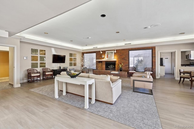 living area featuring visible vents, baseboards, a raised ceiling, ornamental molding, and light wood-style flooring