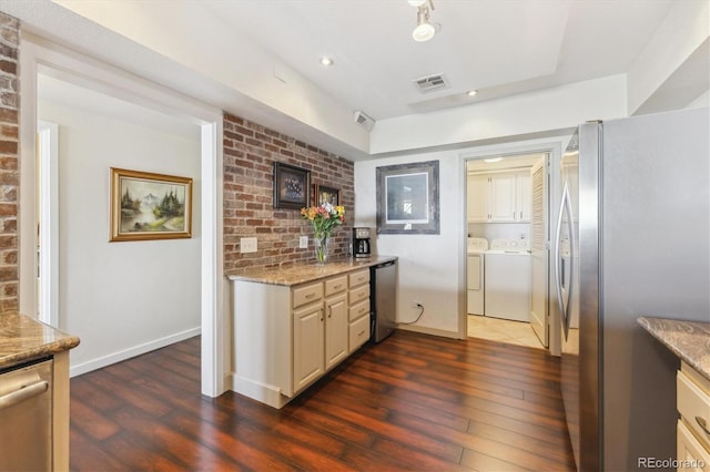 kitchen with visible vents, light stone countertops, dark wood-style floors, washing machine and clothes dryer, and stainless steel appliances