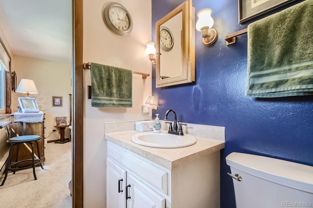 bathroom with toilet, vanity, and a textured wall