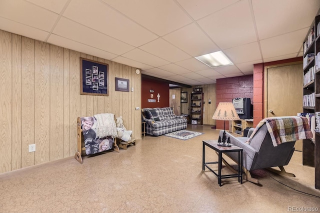 living room featuring a paneled ceiling and wooden walls