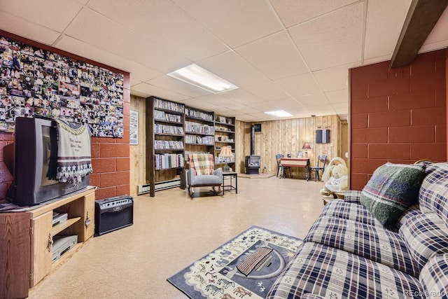 living room with tile patterned floors, concrete block wall, a baseboard radiator, a paneled ceiling, and a wood stove