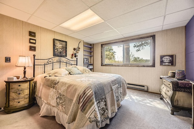 carpeted bedroom with wood walls, baseboard heating, and a drop ceiling