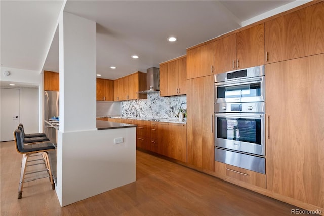 1020 15th St Unit 42A, Denver, CO 80202 - kitchen featuring a warming drawer, stainless steel appliances, wall chimney range hood, light wood-style flooring, and brown cabinets
