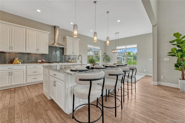 11821 Discovery Ln, Parker, CO 80138 - kitchen featuring wall chimney exhaust hood, light wood-style flooring, a kitchen island with sink, white cabinetry, and recessed lighting