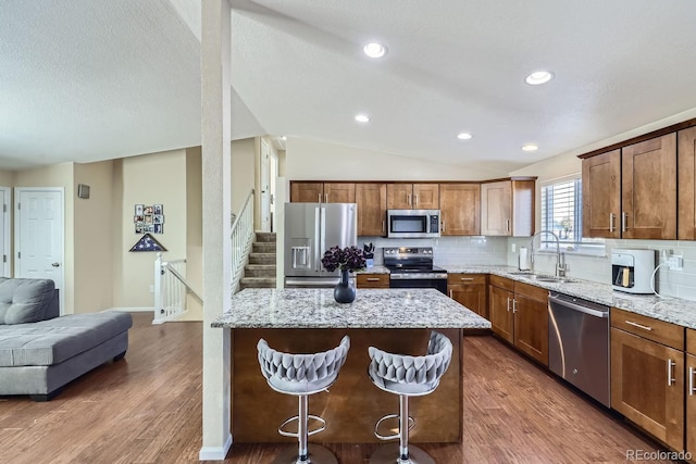 kitchen with sink, light stone counters, vaulted ceiling, appliances with stainless steel finishes, and a kitchen island