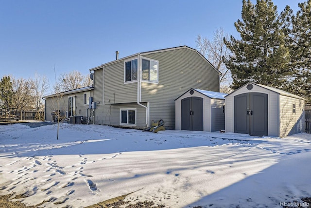 snow covered back of property featuring cooling unit and a shed