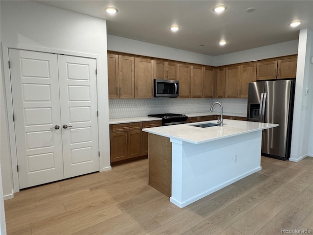 kitchen with sink, light hardwood / wood-style flooring, decorative backsplash, an island with sink, and appliances with stainless steel finishes