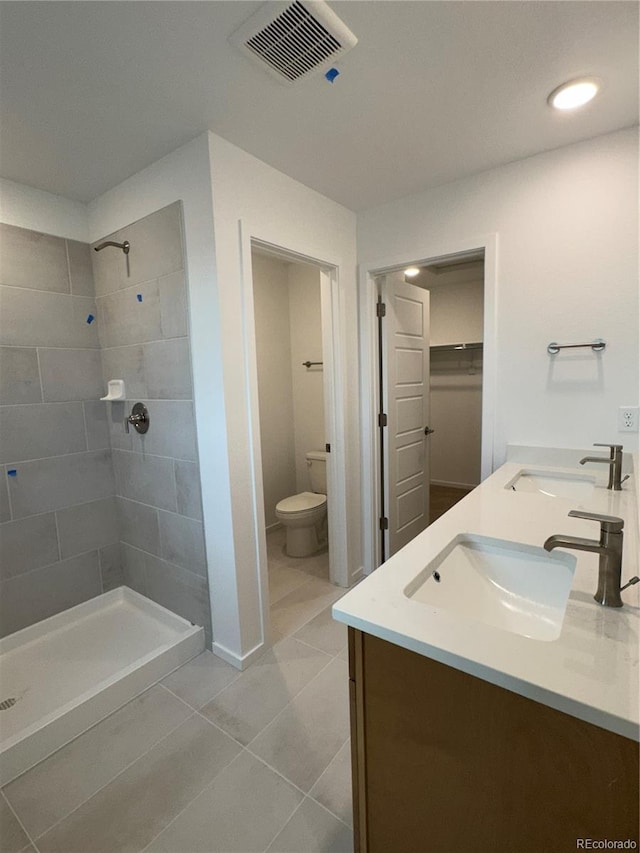 bathroom featuring tile patterned flooring, a tile shower, vanity, and toilet