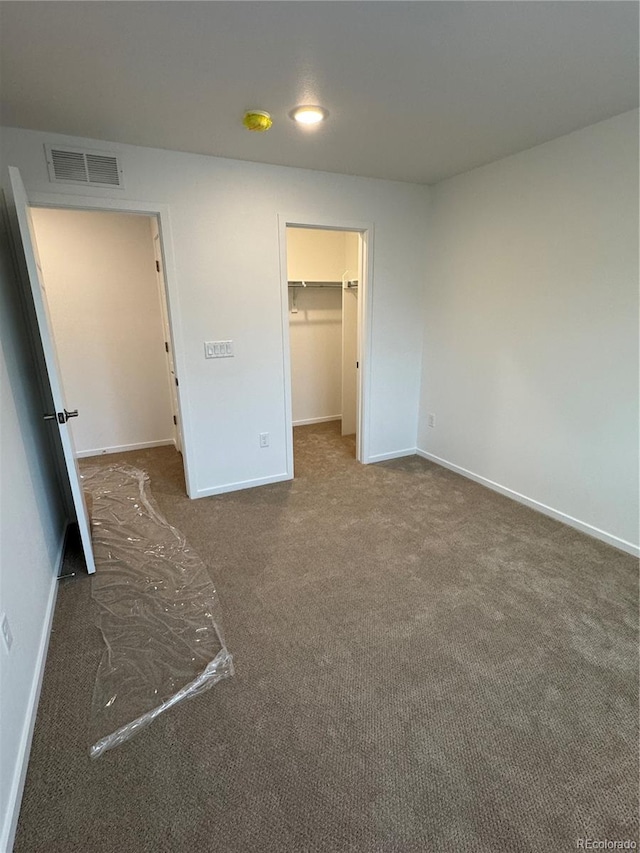 unfurnished bedroom featuring dark colored carpet, a walk in closet, and a closet