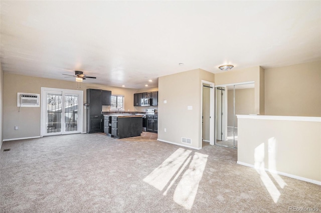 unfurnished living room featuring ceiling fan, light colored carpet, sink, and a wall unit AC