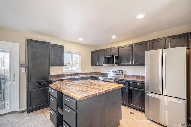 kitchen with light tile patterned flooring, a kitchen island, appliances with stainless steel finishes, butcher block counters, and sink